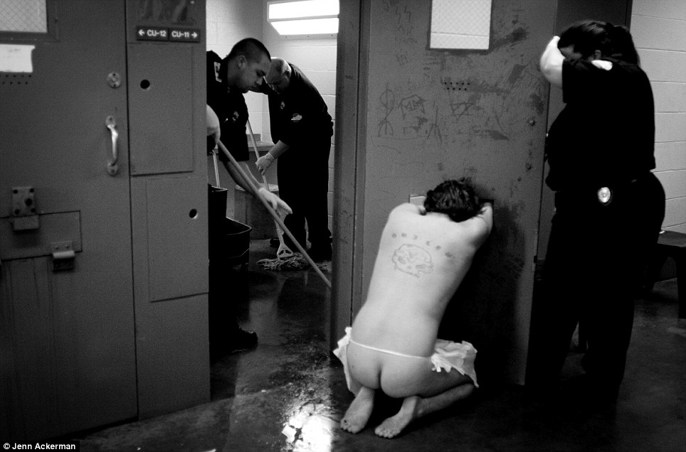 Naked man kneeling with cops trying to get him in, or out, of his cell